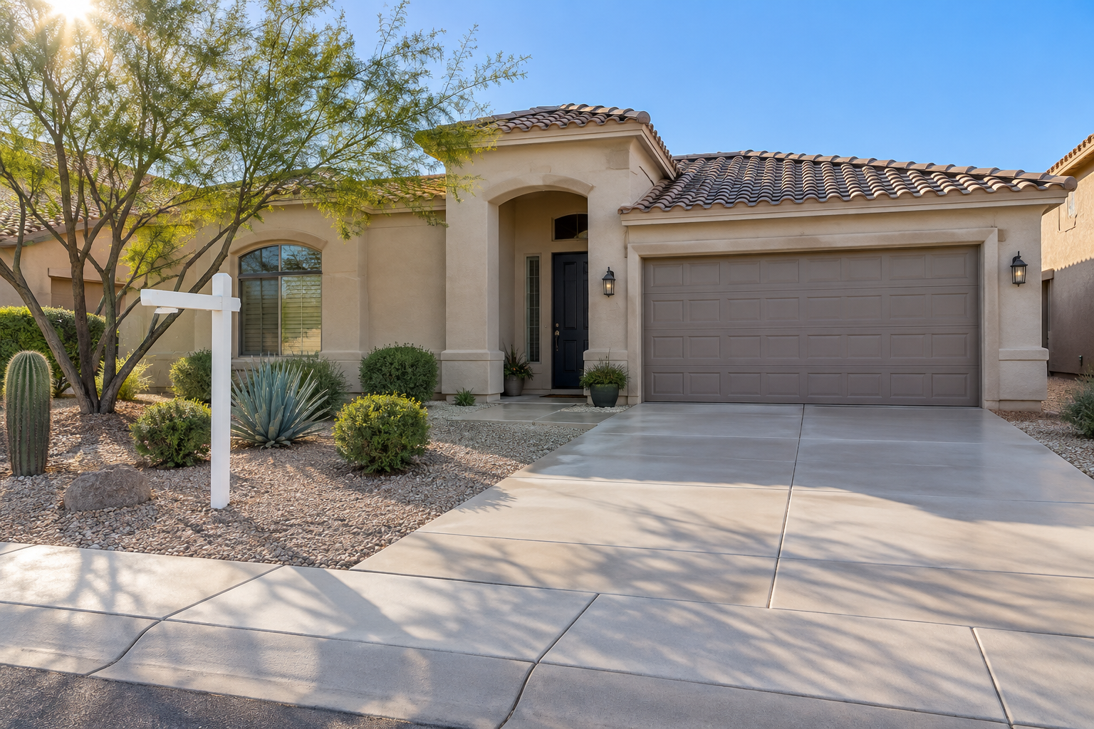 Freshly cleaned concrete driveway and entry of a Scottsdale stucco home with a real estate yard sign, bright morning light